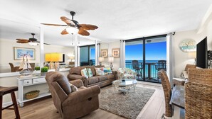 A living room with a sofa, chairs, a coffee table, a ceiling fan, and a view of the ocean.