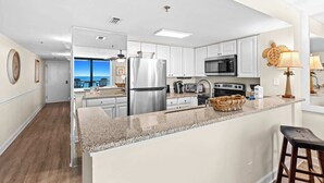 A modern kitchen with white cabinets, stainless steel appliances, and a view to the outside.
