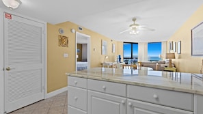 A hotel room with a large window offering a view of the ocean, a ceiling fan, a marble countertop, and a door with a fire exit sign. - SunDestin Resort Unit 0715 (Destin)