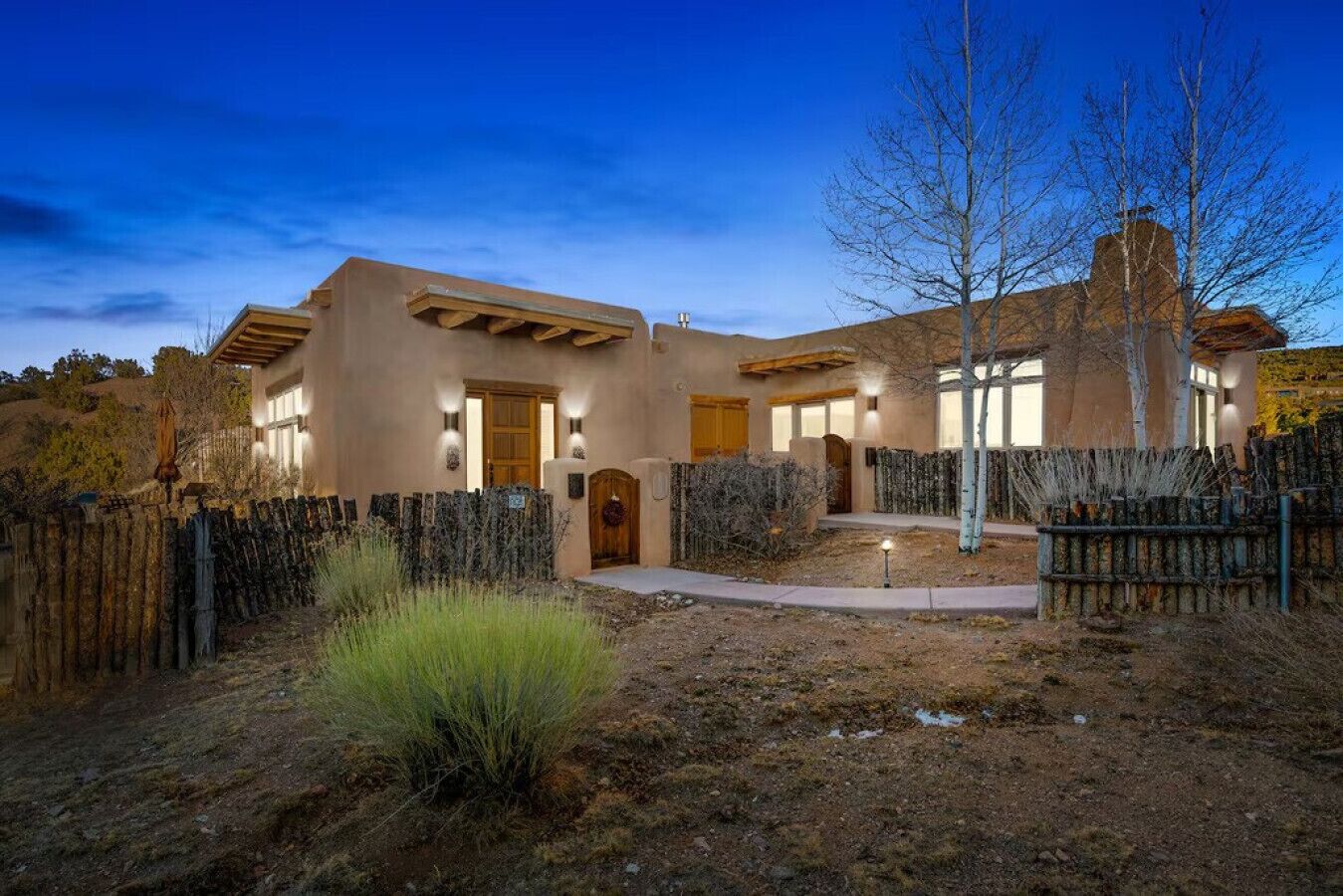 A stucco house with a wooden deck, a front door, and a fenced yard.