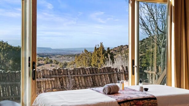 A bedroom with a large window, a bed, and a view of a landscape.