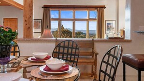 A dining area with a table set for two, a window with a view of the outdoors, and wooden beams on the ceiling.