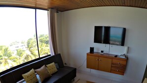 A living room with a sofa, a TV mounted on the wall, a wooden cabinet, and a window with a view of palm trees. - SEA VIEW APARTMENT CLOSE TO THE BEACH (San Andrés y Providencia)