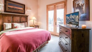 A bedroom with a bed, a dresser, a TV, and a window with blinds.