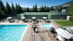 A pool area with a tennis court, lounge chairs, and umbrellas.