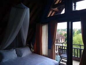 A bedroom with a bed, curtains, and a view of the outside. - Villa Kania by WizZeLa (Nusa Dua)