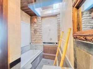 A bathroom with a bathtub, a shower, and a stone wall. - Villa Kania by WizZeLa (Nusa Dua)