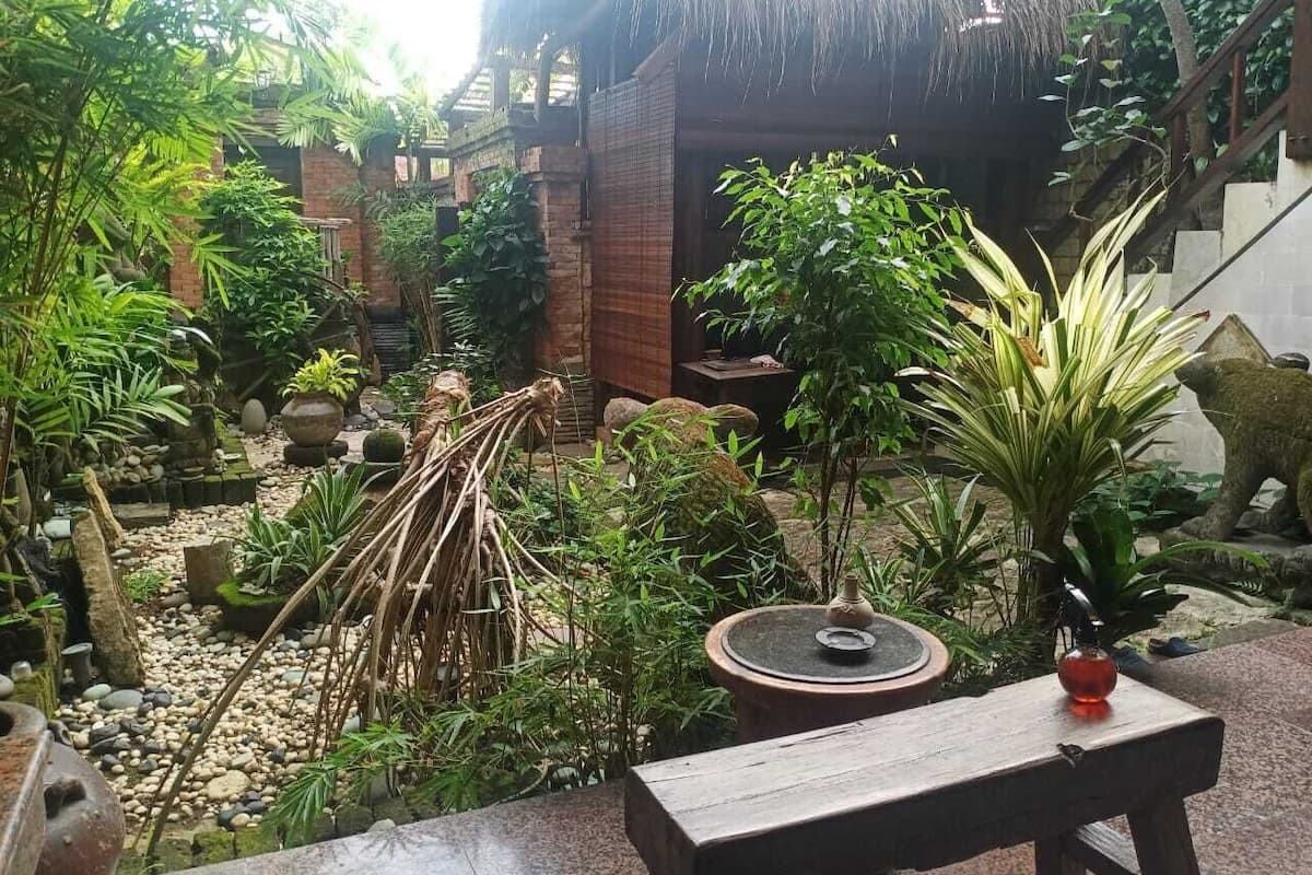 A garden with a thatched-roof structure, a stone bench, and various plants.