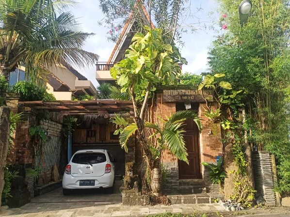A traditional house with a car parked in front, surrounded by lush greenery and a thatched roof structure. - Villa Kania by WizZeLa (Nusa Dua)