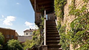 Un escalier en bois mène à un balcon en bois, lequel est bordé d’un côté par un mur de briques.