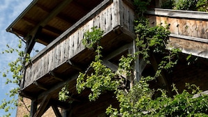 Un balcon en bois, orné de lierre grimpant, adossé à un bâtiment en pierre.