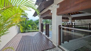 A wooden deck with a glass railing, surrounded by greenery and a clear sky. - Harmony Villa Dua (Kerobokan)