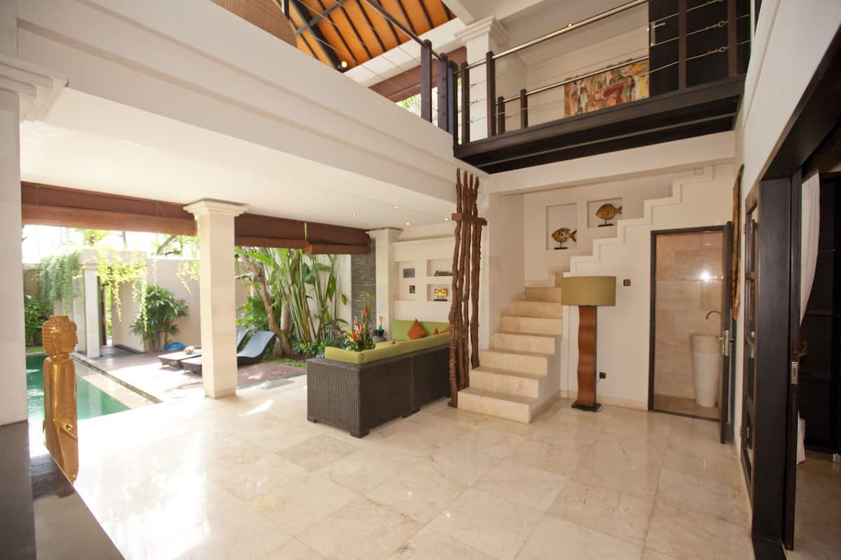 Un vaste espace intérieur comprenant une piscine, un escalier et un coin salon agrémenté de plantes.