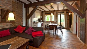 A cozy living room with a dark brown sofa, red cushions, and a wooden coffee table. A dining area with a wooden table and chairs is visible in the background. - Storage N ° 1 - Lily (Waren (Müritz))