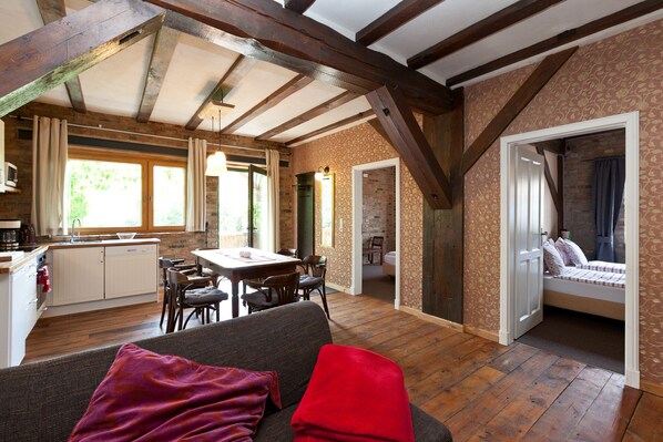 Ein rustikales Interieur mit freiliegenden Holzbalken, einem Essbereich, einer Küche und einer gemütlichen Sitzecke mit Blick ins Freie.