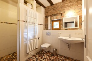 Ein Badezimmer mit gefliestem Boden, einer weißen Toilette, einem Waschbecken und einem Spiegel.