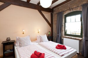 Ein Doppelbett mit gestreifter Bettwäsche, ein Nachttisch mit Lampe und ein Fenster mit Vorhängen.