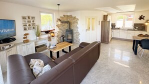 Een moderne woonkamer met een bruine leren bank, een houten eettafel en een keuken met witte kasten en een fornuis.