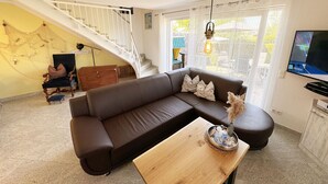 Een woonkamer met een bruine modulaire bank, een houten salontafel, een trap en een televisie aan de muur.