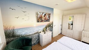Een slaapkamer met een strandmuur, een groene stoel, een witte dressoir en een garderobe.