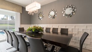 Une salle à manger avec une table en bois foncé, des chaises noires et un miroir décoratif doté d’un cadre circulaire.