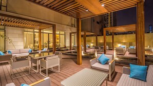 An outdoor patio area with wooden flooring, seating arrangements, and a water feature.