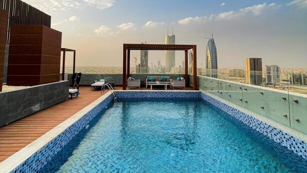 A rooftop pool with a city view, lounge chairs, and a wooden deck.
