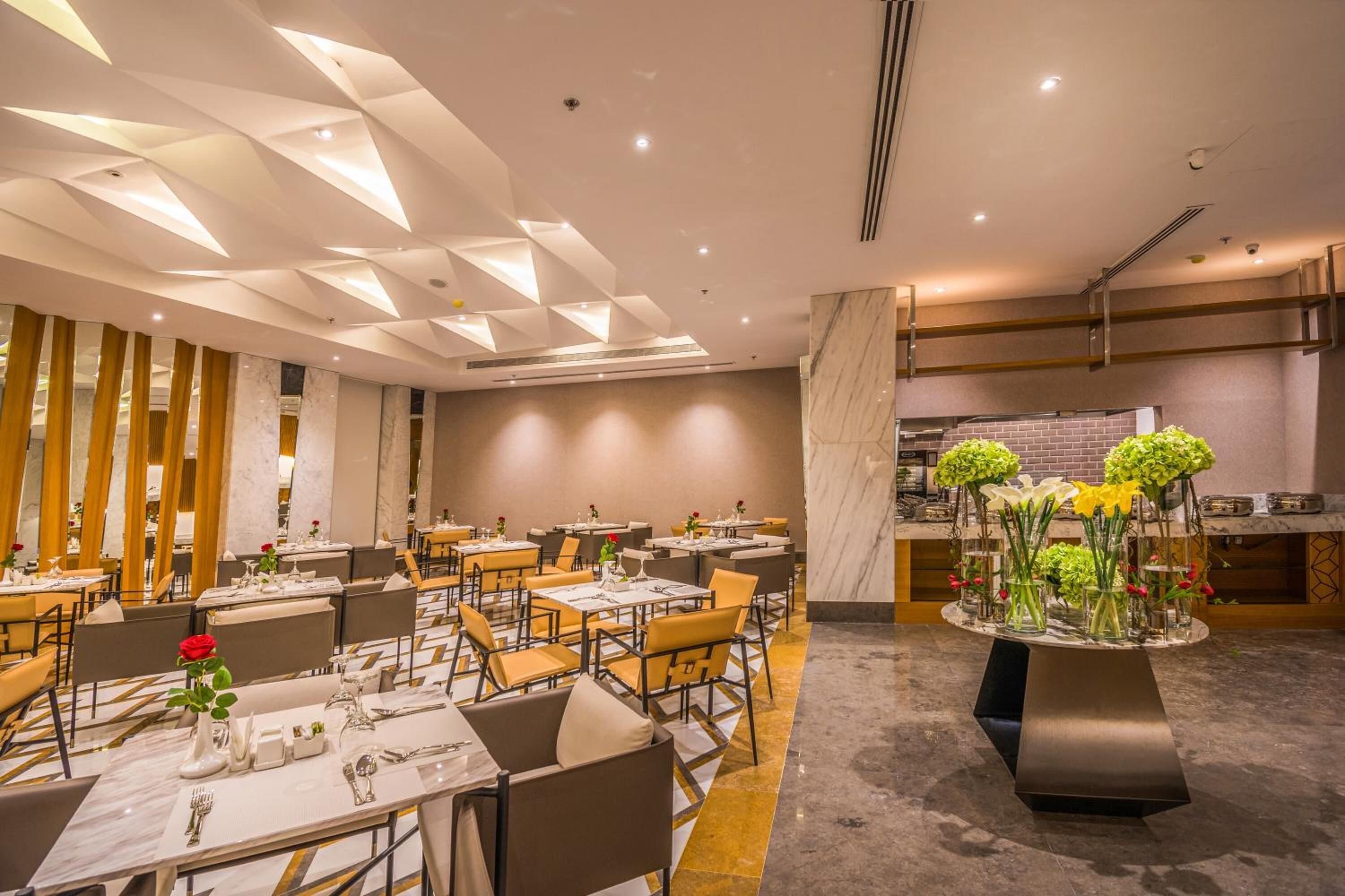 A modern restaurant with a geometric ceiling design, marble flooring, and a central floral arrangement.