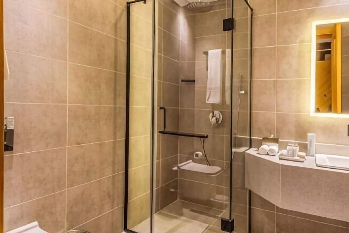 Un baño moderno con ducha de vidrio, lavamanos blanco con artículos de aseo y espejo con marco de madera.