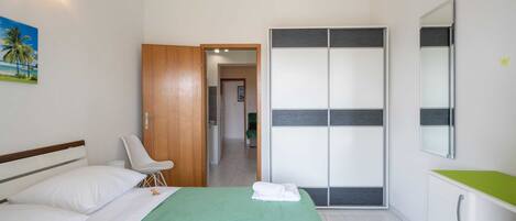 Habitación de hotel con cama, una silla, armario y un baño visible a través de una puerta abierta.