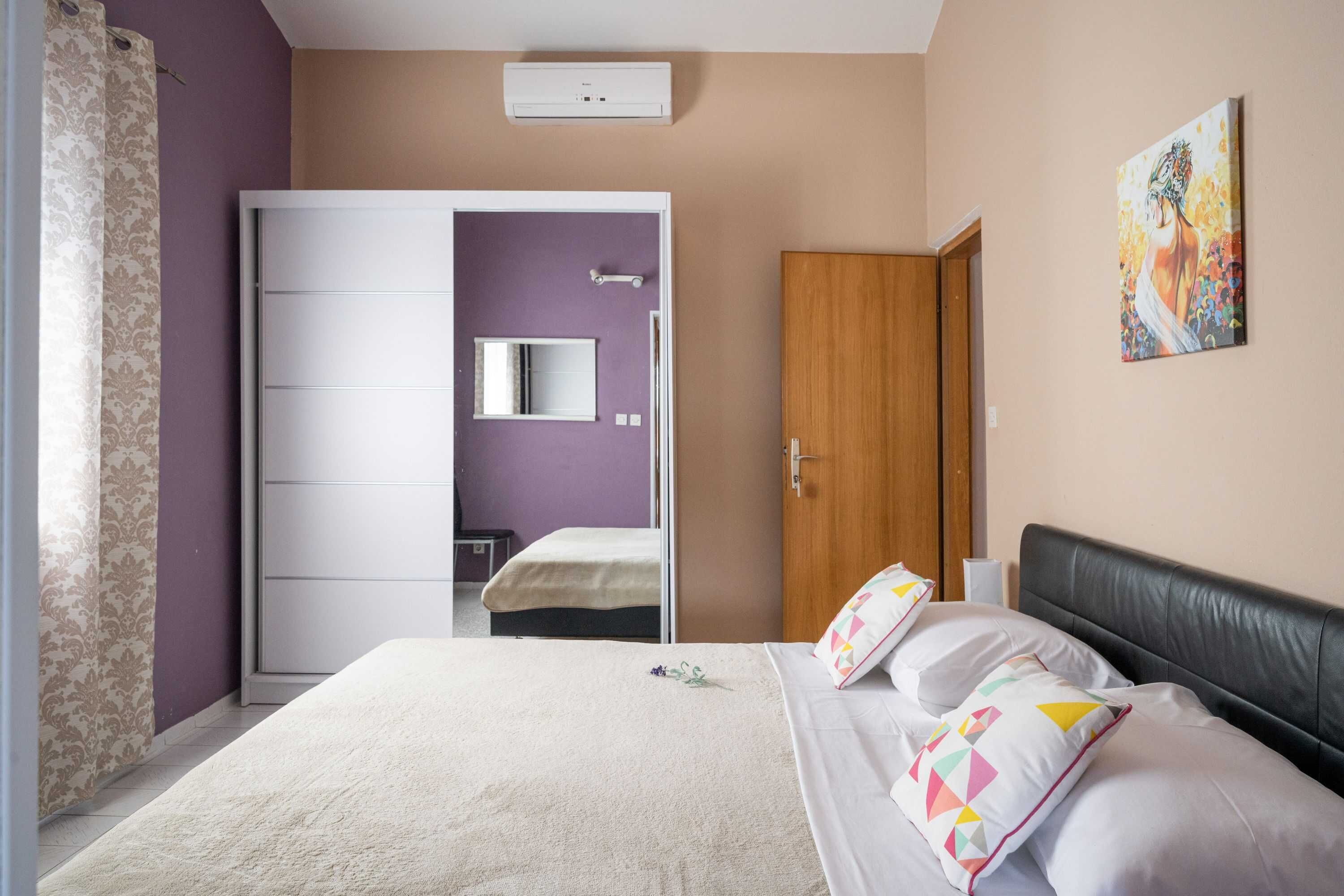 A bedroom with a bed, a wardrobe, a bathroom, and a painting on the wall.