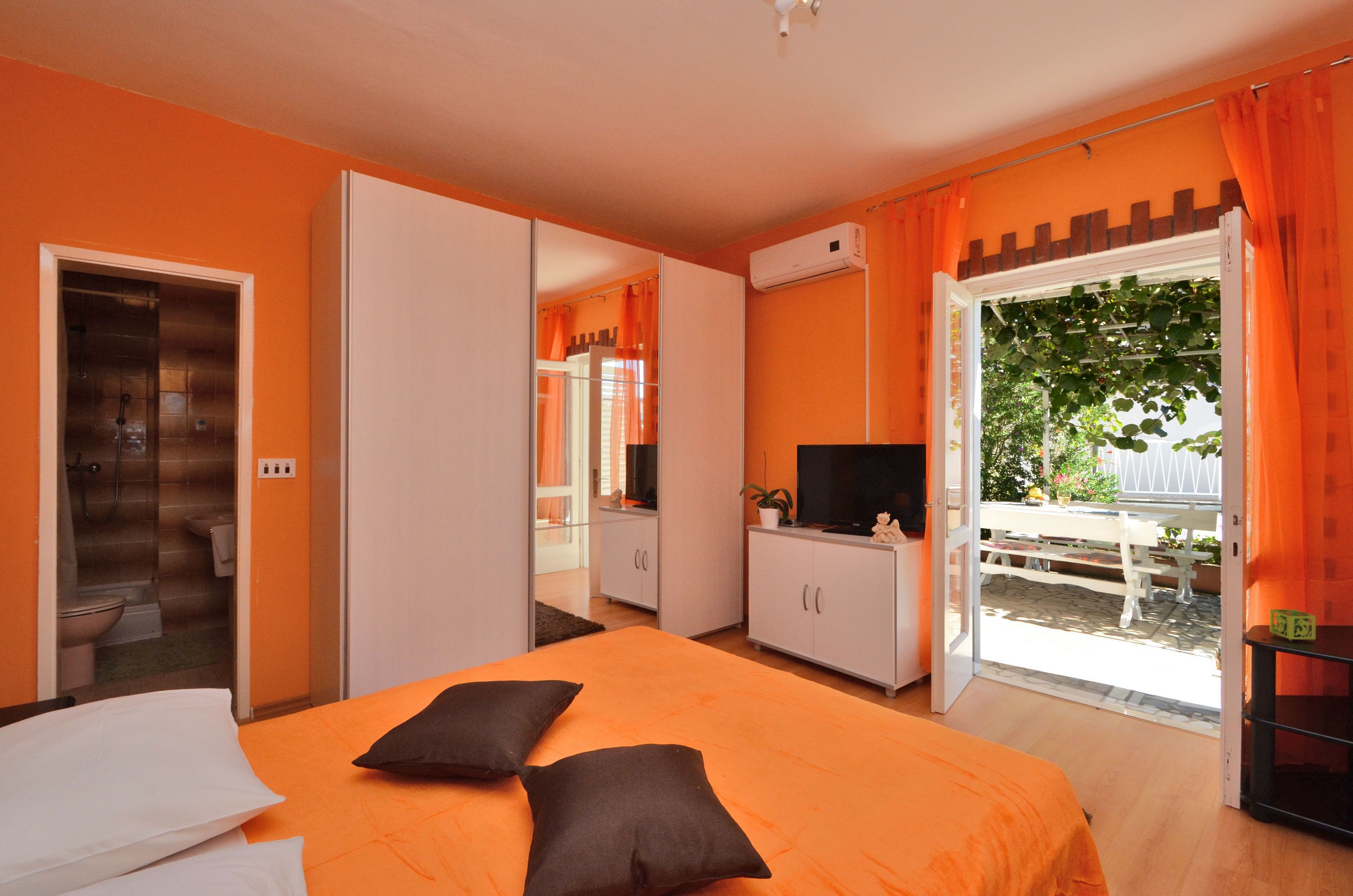 A room with an orange bed, white wardrobe, and a TV on a cabinet.