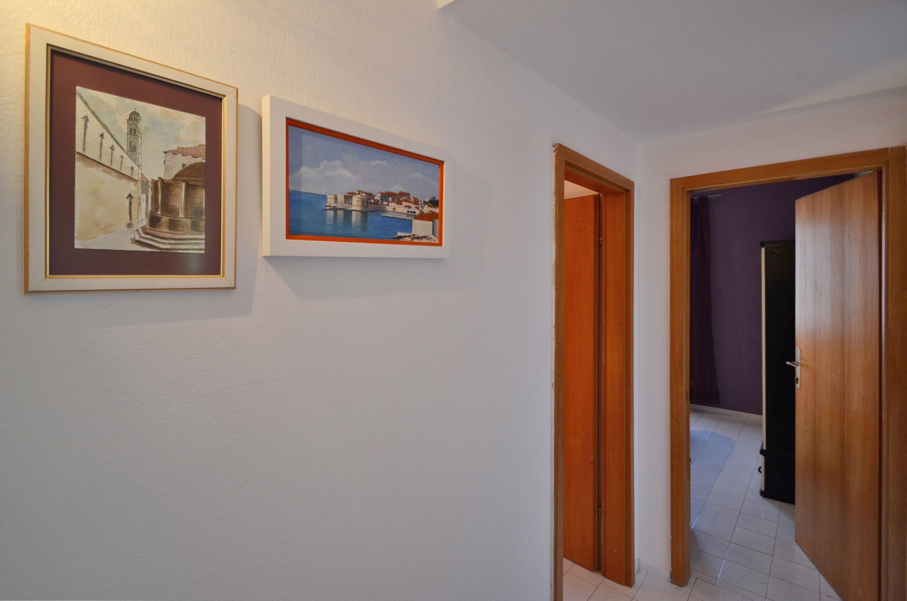 A hallway with two framed paintings on the wall, a wooden door, and a view into a room with purple walls.