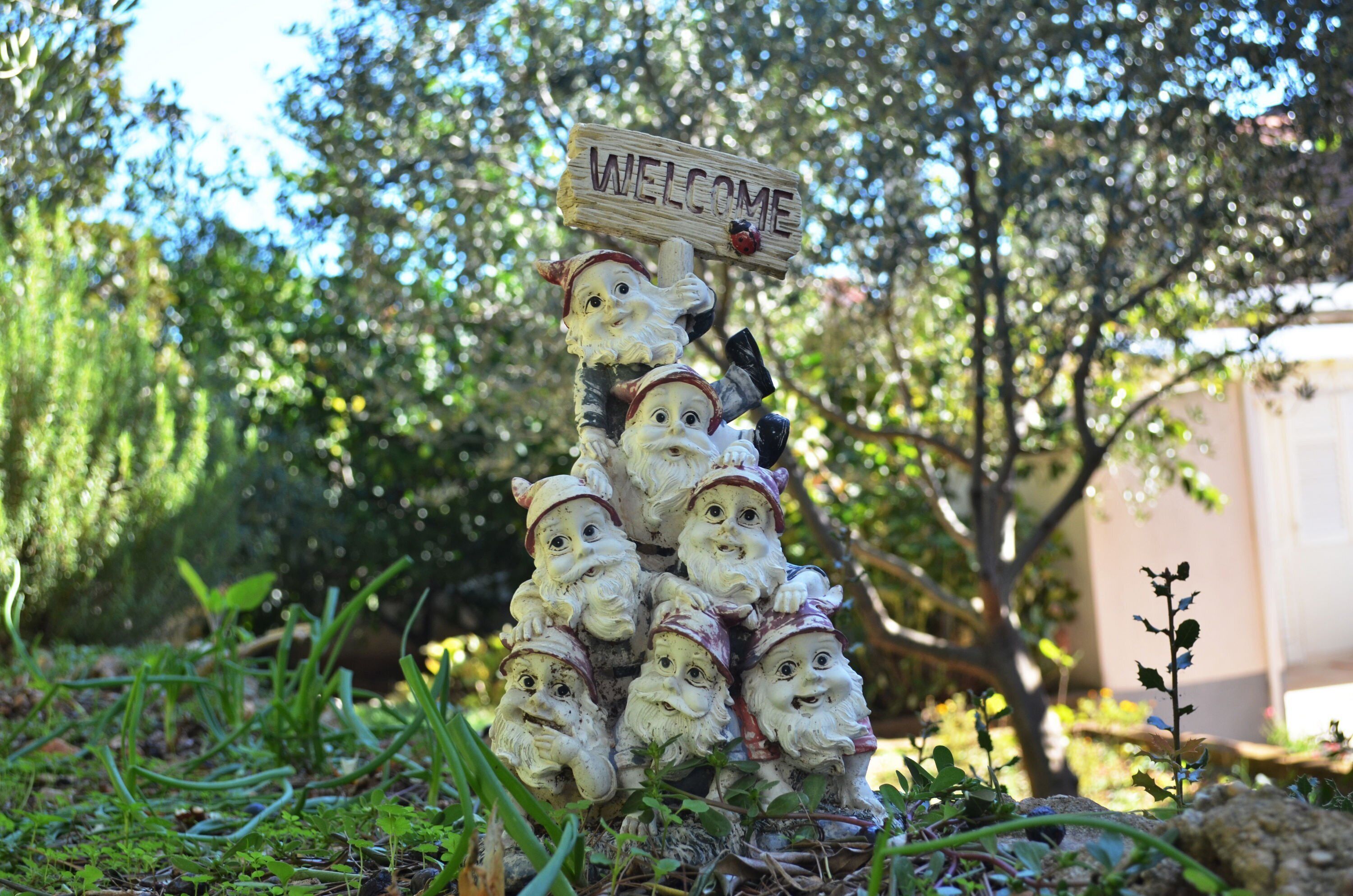 A decorative welcome sign with a wooden texture and a ladybug sticker, surrounded by garden gnomes.