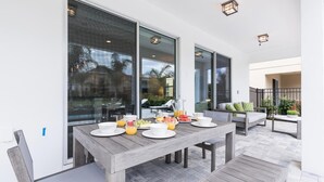 An outdoor dining area with a wooden table set for breakfast, large windows, and a view of the backyard. - Ultimate 5 Star Villa with Private Pool on Encore Resort at Reunion, Orlando Villa 4363 (Orlando)