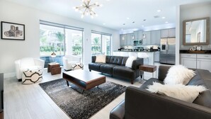 A modern living room with a black leather sofa, a white armchair, and a coffee table. There is a kitchen in the background with stainless steel appliances. - Ultimate 5 Star Villa with Private Pool on Encore Resort at Reunion, Orlando Villa 4363 (Orlando)