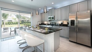 A modern kitchen with a central island, stainless steel appliances, and a large window overlooking a garden. - Ultimate 5 Star Villa with Private Pool on Encore Resort at Reunion, Orlando Villa 4363 (Orlando)