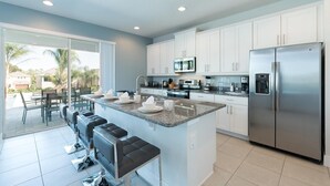 A modern kitchen with white cabinets, a stainless steel refrigerator, and a central island with bar stools. - Ultimate 5 Star Villa with Private Pool on Encore Resort at Reunion, Orlando Villa 4365 (Orlando)