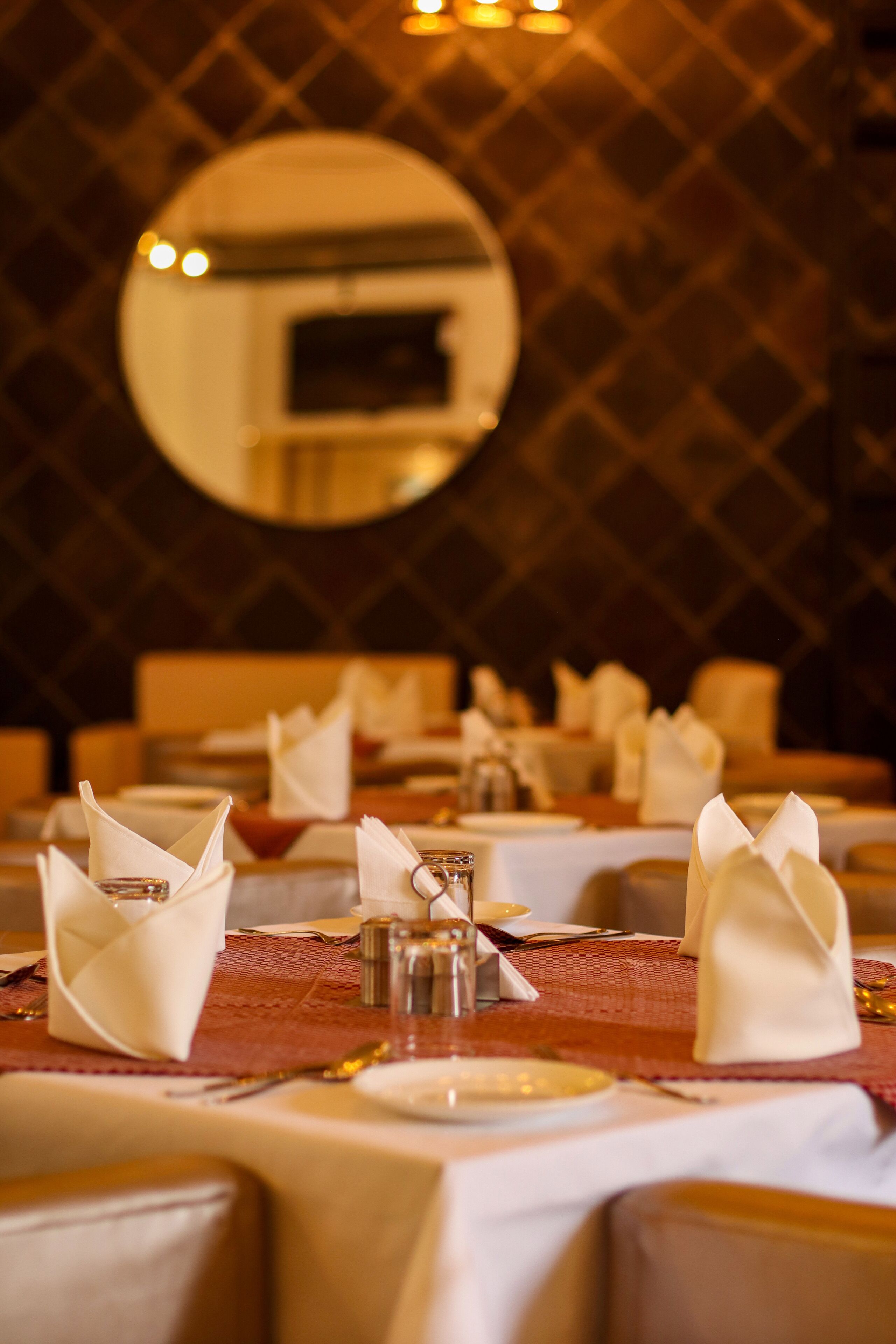 A restaurant setting with tables set for dining, including folded napkins and salt and pepper shakers.
