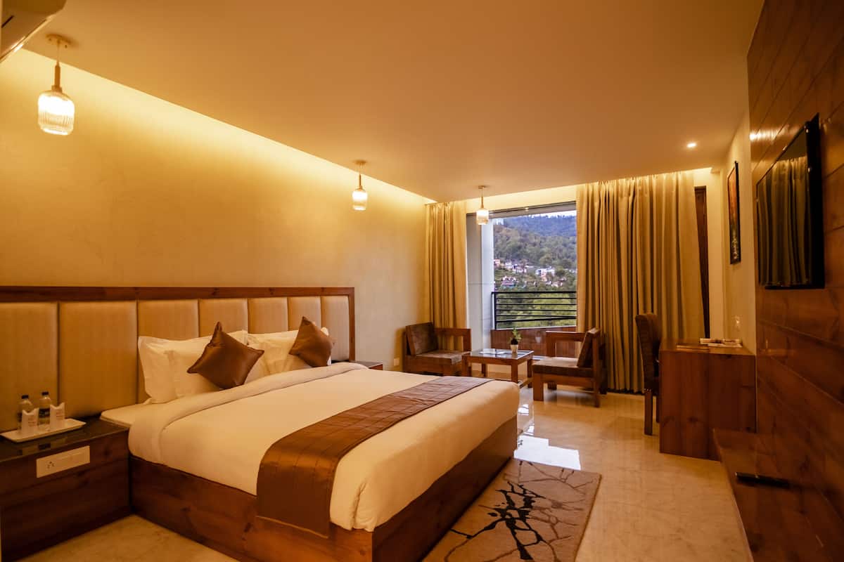 A hotel room with a large bed, a desk, a chair, a TV, and a window with curtains.