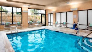 Una piscina interior con agua cristalina, rodeada de sillones de descanso y un muro de piedra.