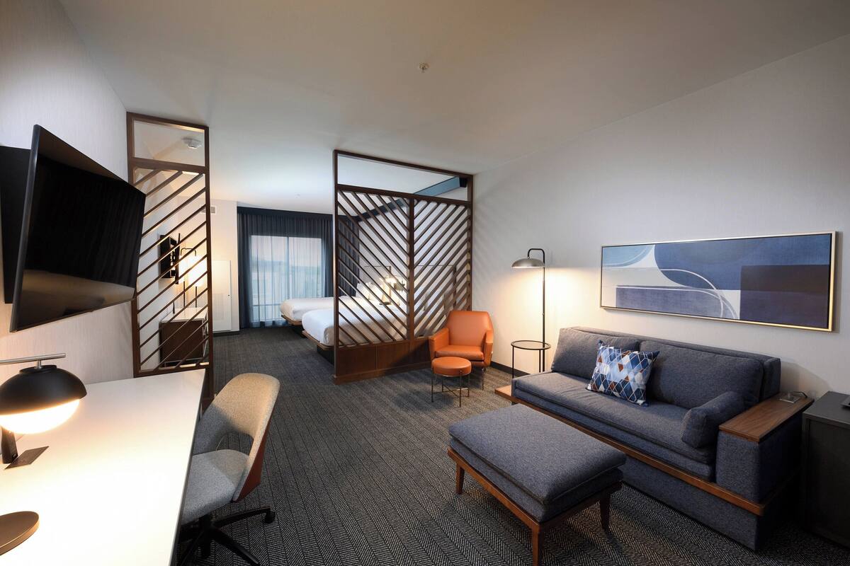 Une chambre d’hôtel avec un lit, un canapé, un bureau, une chaise, une télévision et un tableau au mur.