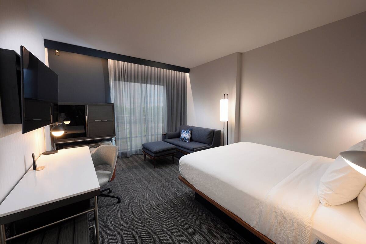 Une chambre d’hôtel avec un lit, un bureau, une chaise, une télévision et une lampe.