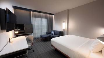 A hotel room with a bed, a desk, a chair, a TV, and a lamp.