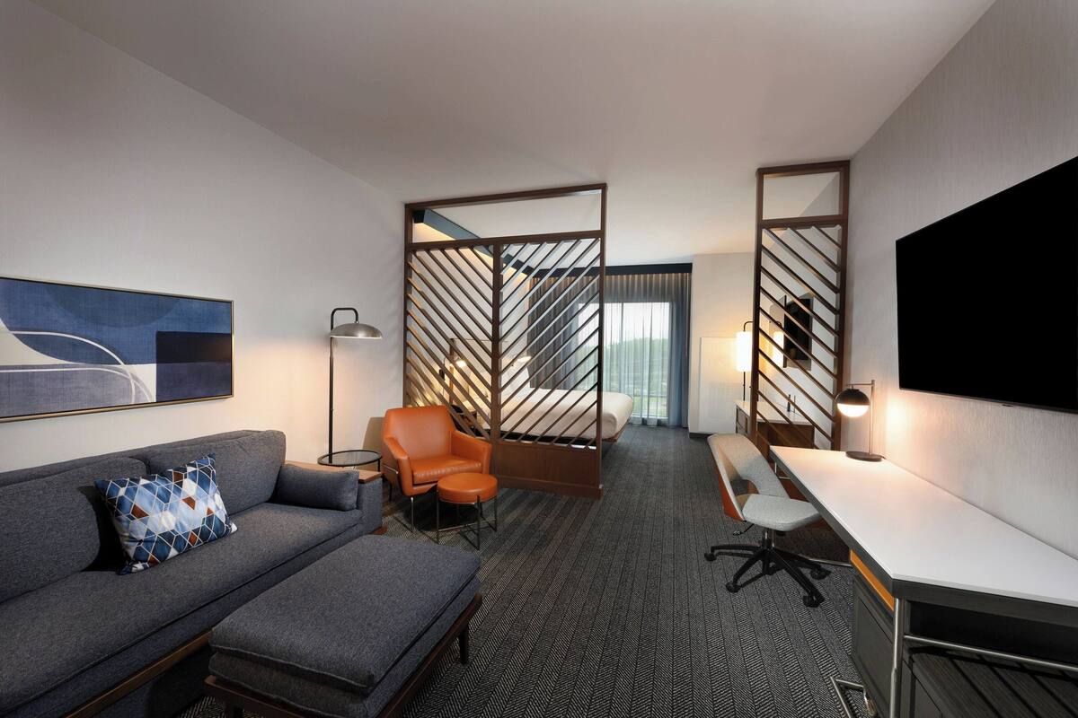 Une chambre d’hôtel équipée d’un canapé, d’un bureau, d’une chaise, d’un lit et d’un grand téléviseur.