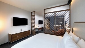 Una habitación de hotel moderna con una cama grande, un televisor de pantalla plana en la pared, un aparador de madera, un escritorio con una silla y un separador con diseño diagonal.
