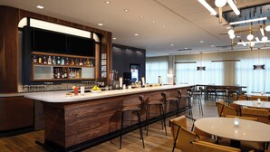 Un área de bar moderna con mostrador de madera, varias opciones de asientos y una pantalla grande sobre la barra.