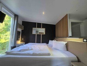 A modern hotel room with a large bed, a bedside table, a mirror, and a window with curtains.