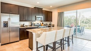 A modern kitchen with dark wood cabinets, stainless steel appliances, a granite countertop, and a large island with bar stools. - Exclusive Villa with Large Private Pool on Encore Resort at Reunion, Orlando Villa 4383 (Kissimmee)