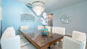 A dining room with a wooden table, white chairs, a chandelier, and wall art. - Exclusive Villa with Large Private Pool on Encore Resort at Reunion, Orlando Villa 4383 (Kissimmee)